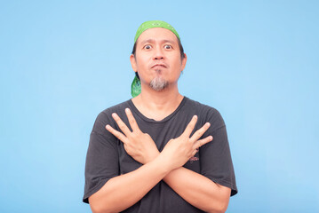 An intense middle-aged barista with wide eyes doing a W hand sign while his arms are crossed against his chest. Isolated on a blue background.