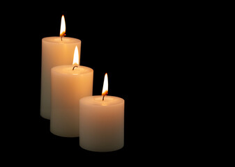 Three burning white candles with different size isolated on black background.