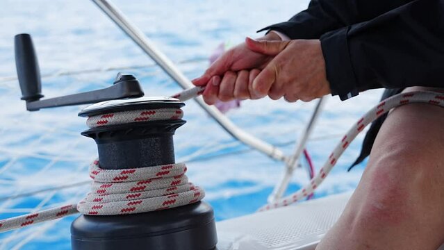 Mans hand pulling winch rope on sailing boat