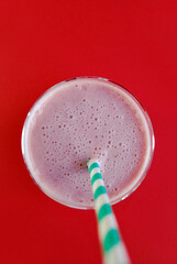 Strawberry and banana pink smoothie in a transparent glass on red background, top view. Milk Shake. Healthy breakfast