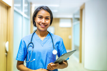 Portrait of smiling asian nurse or female doctor health worker wearing blue uniform holding digital tablet while posing on modern hallway clinic. healthcare workers