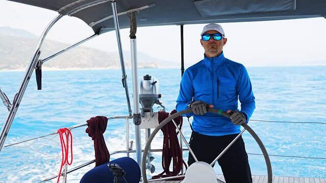 Young man captain stands at the helm and controls a sailboat during a journey by sea
