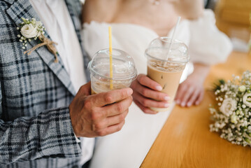 Young couple drinking ice coffee through a straw on wedding day in a cafe. The bride and groom holding a cocktail in her hand. Closeup.