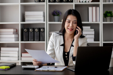 Beautiful asian woman talking on the phone, businesswoman working in office attentively to grow and modernize start-up business, she is analyzing company's market and financial data.