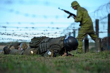 Fully equipped soldier crawling under barbed wires overcoming obstacle course. Ukraine