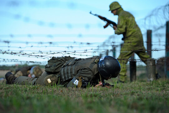 Fully equipped soldier crawling under barbed wires overcoming obstacle course. Ukraine