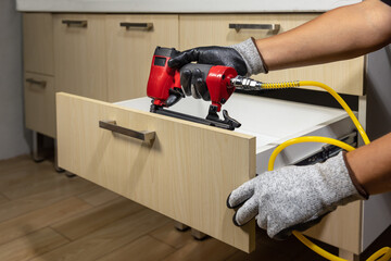 Worker repair wooden drawer of cabinet with pneumatic nail gun.