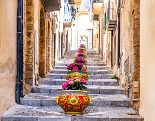 Narrow street in the old town of Cefalu, medieval village on Sicily island, Italy. Flower pots with...