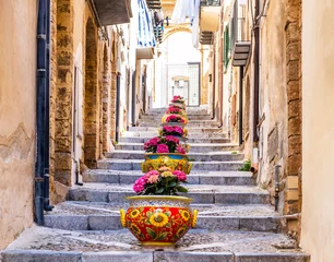 Zelfklevend Fotobehang Palermo Narrow street in the old town of Cefalu, medieval village on Sicily island, Italy. Flower pots with traditional sicilian decoration. La Rocca cliff. Popular tourist attraction in Province of Palermo