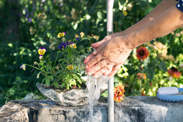 Washing hands. Old woman washing her hands in the garden. Hygiene and Cleaning Hands. 