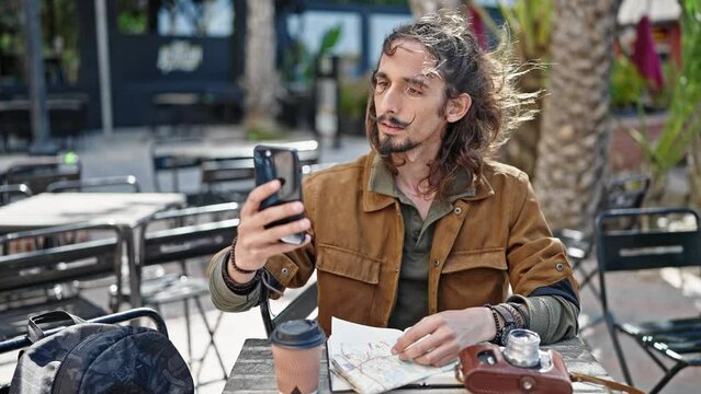 Young hispanic man tourist make selfie by smartphone sitting on table at coffee shop terrace