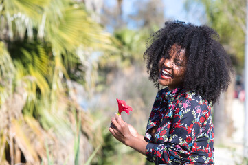 Young, beautiful black woman with afro hair holds a red flower in her hands. The beautiful woman is happy and smiling.