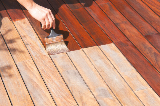 Ipe wood worker's hand is oiling terrace decking with a painting brush