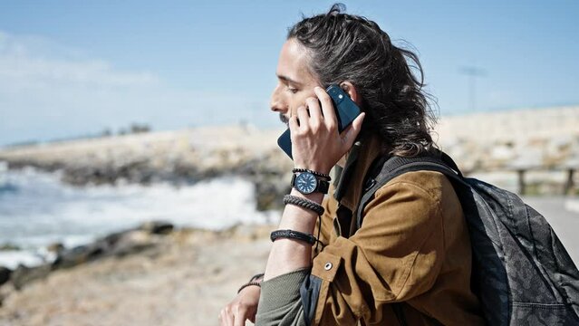 Young hispanic man tourist wearing backpack talking on smartphone at seaside