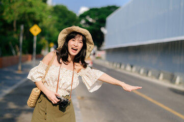 Portrait of asian young woman traveler with weaving hat and basket and a camera waving hand to friend by the street. Journey trip lifestyle, world travel explorer or Asia summer tourism concept.