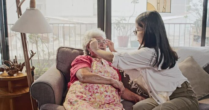 Cute Latina teenager fixes her beautiful grandmother's glasses with a lot of love while she spends a good time with her sitting on the couch in the living room.
