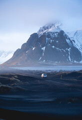 Un camping-car blanc en train de voyager sur un sol rocheux devant les montagnes.