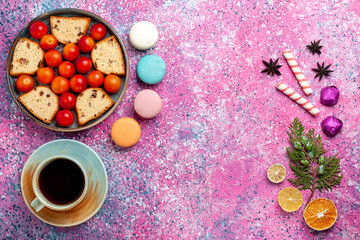 top view delicious sliced cake with sour fresh plums macarons and cup of tea on the pink background pie sweet bake biscuit cookie fruits