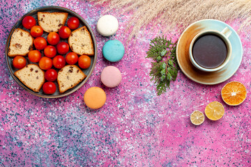 Obraz na płótnie Canvas top view delicious sliced cake with sour fresh plums macarons and cup of tea on the pink desk pie sweet bake biscuit cookie sugar fruits