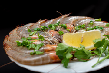 On a white plate large fresh shrimp with lemon and herbs