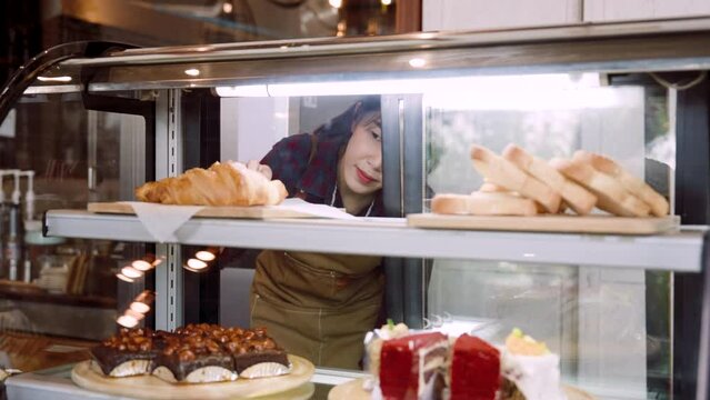 Shop owner is checking bakery, open candy cabinet bend down count number treats in cabinet, in order receive orders online that people have ordered, before confirming order be ready be delivered.