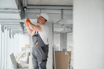 Man setting up ventilation system indoors. A male worker installs air ventilation pipes in a new office building.