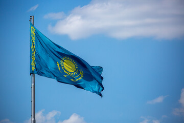 The flag of Kazakhstan is fluttering in the wind against the blue sky. The flag is located on the blue dome of the administrative building. The city of Astana is the administrative center.