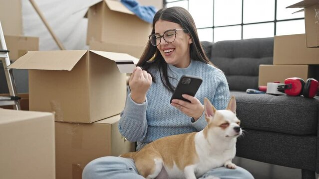 Young hispanic woman with chihuahua dog using smartphone and credit card at new home