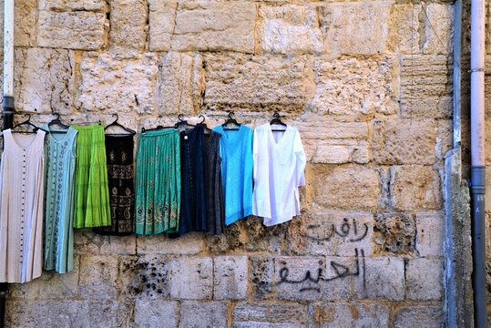Clothes hanging in Jerusalem marketplace, incidental graffiti on wall reads:  "praise Hanifah" [Hanifah is a girl's name, derivative name is Latifah].