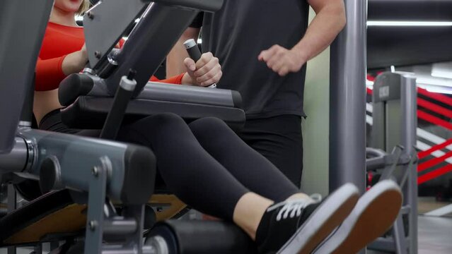 Closeup coach man guidance workout with leg muscles stretch with equipment machine with woman in fitness gym club, strength and training, woman exercise with instructor or trainer, sport concept.