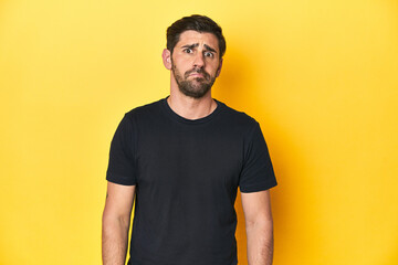Caucasian man in black t-shirt, yellow studio backdrop sad, serious face, feeling miserable and...