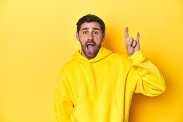 Man in yellow hoodie, monochrome studio backdrop showing a horns gesture as a revolution concept.