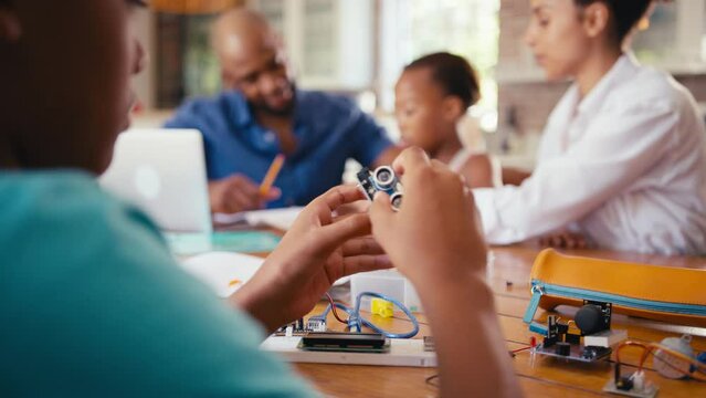 Family around table at home using laptop with parents helping children with STEM based homework on electronics project with focus pulled from background to foreground - shot in slow motion