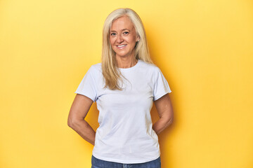 Middle-aged Caucasian woman in white t-shirt, yellow studio happy, smiling and cheerful.