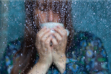 mujer bebiendo de una taza de café detrás de cristal con gotas con vestido azul