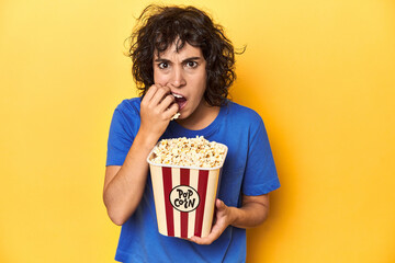 Engaged woman with popcorn watching screen, home cinema concept, yellow studio backdrop.
