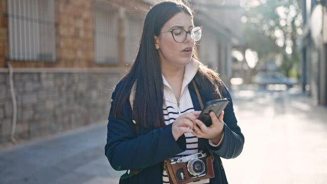Young hispanic woman tourist wearing backpack using smartphone at street