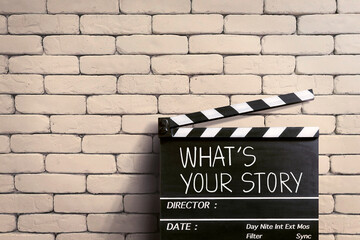 what's your story. handwritten on clapperboard or film slate. white brick wall.