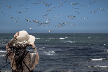 Girl looking at the seagulls and holding her hat in a windy day at Angeiras beach, Matosinhos,...