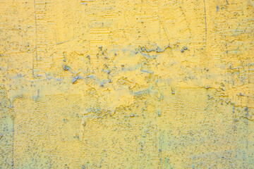 Fragment of the outer wall of an old house with rough plaster. Gray and blue bumps show through the new yellow paint. Background. Texture. Close-up.