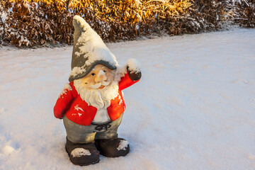 Close up view of cute figure of gnome standing in snow covered garden on sunny frosty winter day....