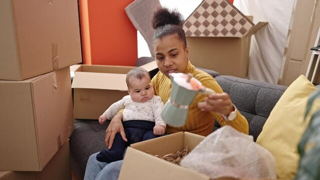 Mother and son sitting on sofa unpacking cardboard box at new home
