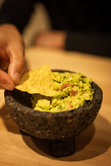 Vertical image of person's hand holding tortilla chip for guacamole dip