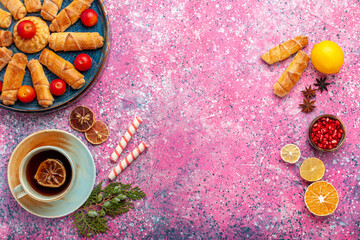 top view sweet delicious bagels inside tray with plums and tea on light pink desk pastry cake biscuit cookies sweet sugar
