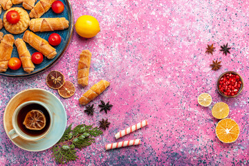 top view sweet delicious bagels inside tray with plums and tea on the pink desk pastry cake biscuit cookies sweet sugar