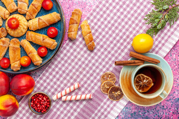 top view sweet delicious bagels inside tray with plums peaches and cup of tea on light-pink desk cake biscuit cookie sweet sugar pie