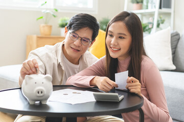 Happy asian young couple love hand putting coin in ceramic piggy bank for saving money to buy real...