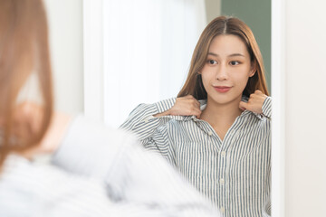 Get dress, pretty asian young woman, businesswoman standing wearing striped shirt, female getting dressed preparing before go to work looking reflection in the mirror in the morning at home.