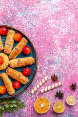 top view sweet delicious bagels inside tray with sour plums on the light pink desk cake biscuit cookie sweet sugar pie