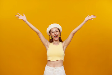 Happy cheerful teen asian woman with raised hands celebrating success isolated on yellow background.